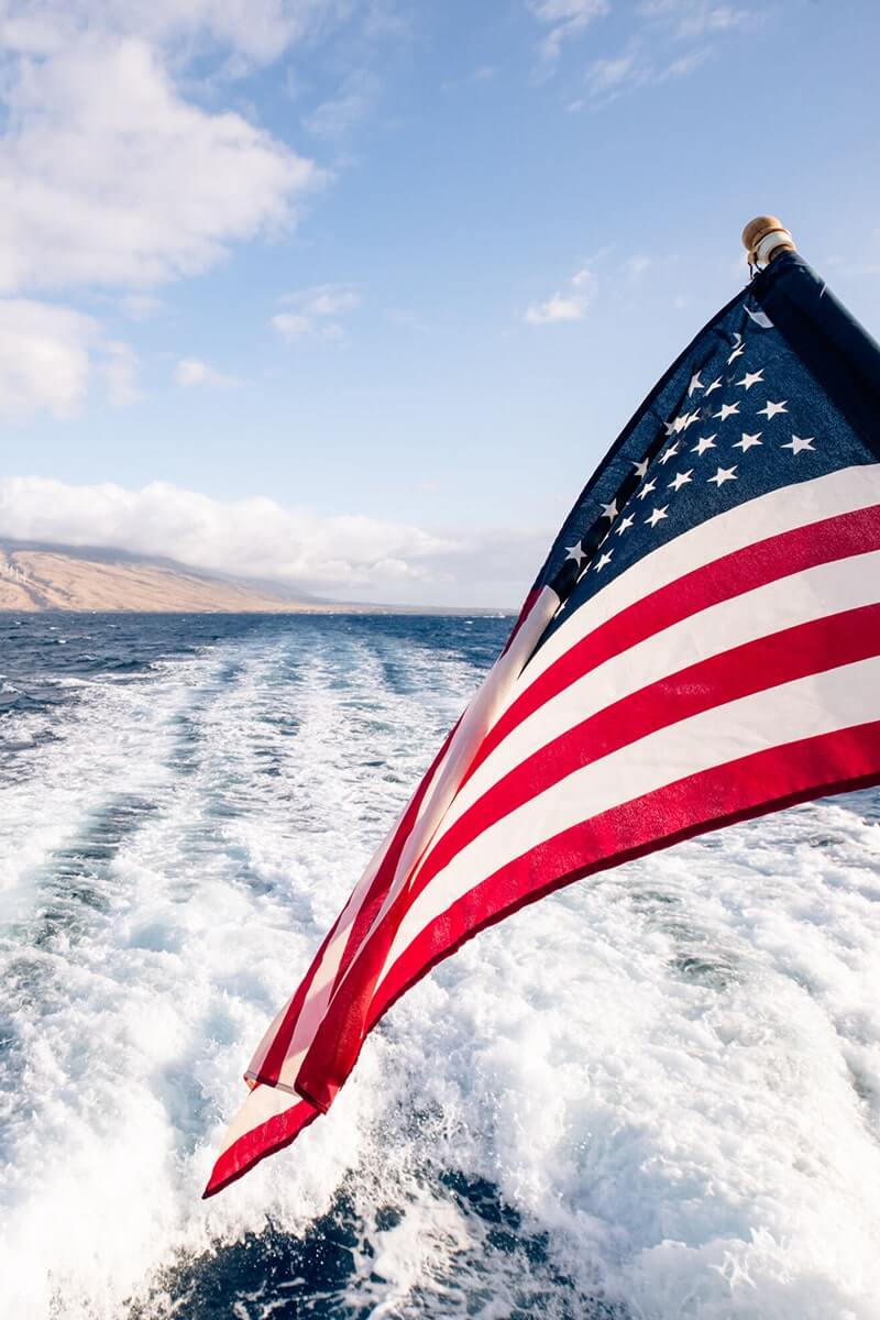 American flag waving with ocean and island in background.