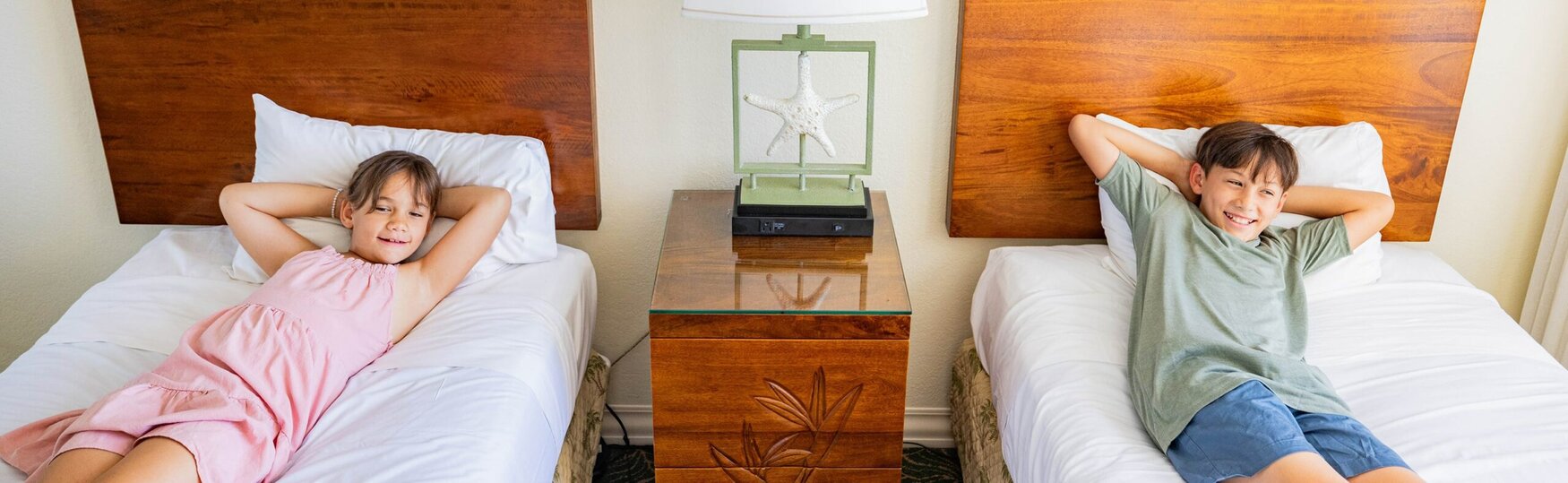 A boy and a girl lying on twin hotel beds.